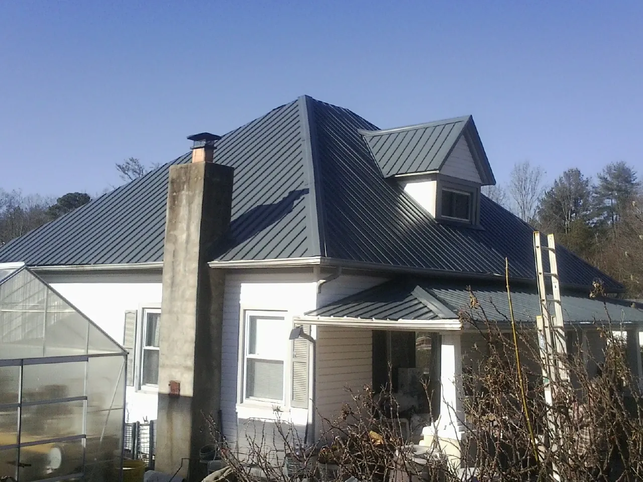 Dark blue standing seam metal roof on a white farmhouse with dormer — Slate & Tile Roof Repair by Roofing Brothers in Hammondsport