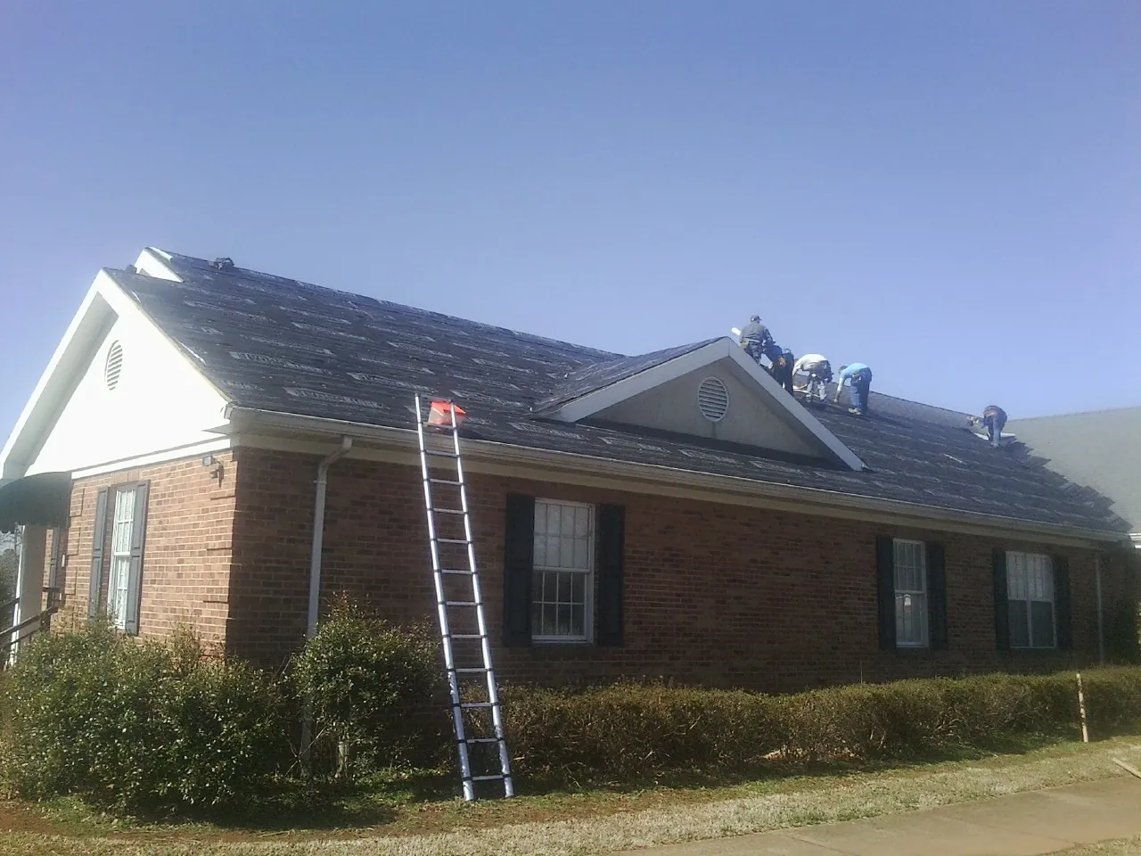 Crew tearing shingles off a brick ranch roof with a ladder set — Emergency Roof Repair work by our crew in Hammondsport