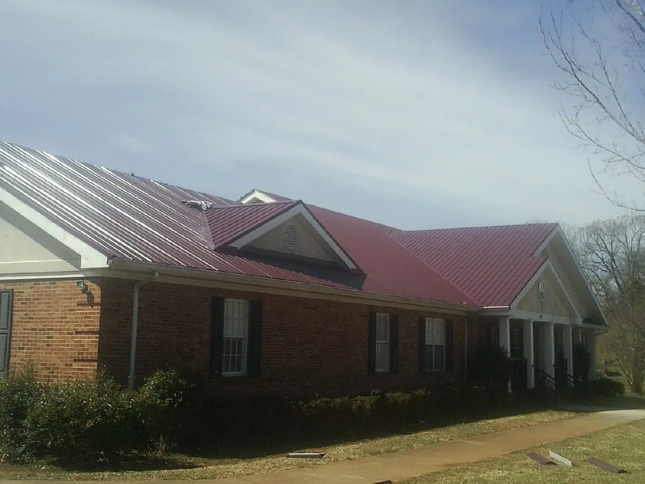 Red metal roof with gabled entries on a long brick building, from a Hail Damage Roof Repair job in Hammondsport