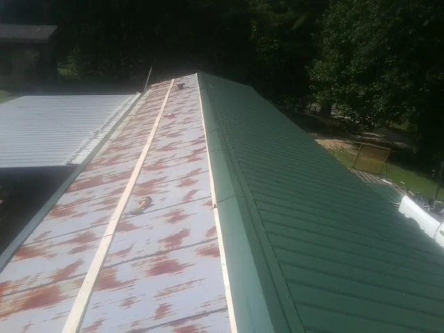 Old rusted panels beside newly installed green metal roofing — Wind Damage Roof Repair by Roofing Brothers in Hammondsport