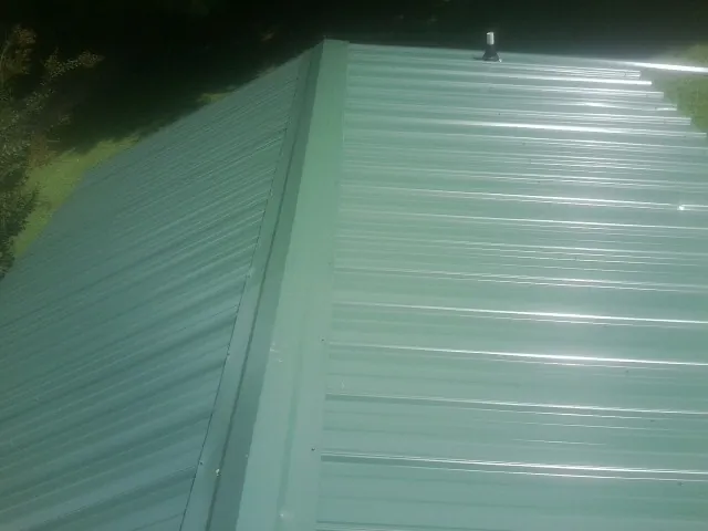 New green metal panels meeting at the ridge of a roof — Flat Roof Repair work by our crew in Hammondsport