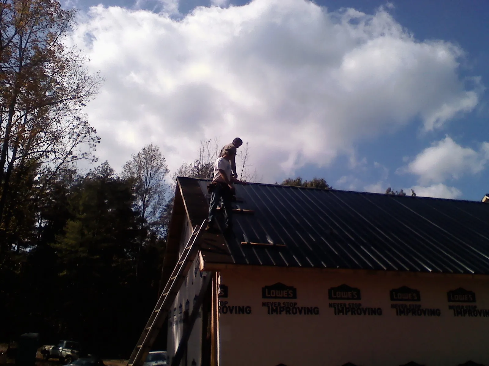 Roofer fastening dark metal panels high against a cloudy sky, from a Roof Inspection job in Hammondsport