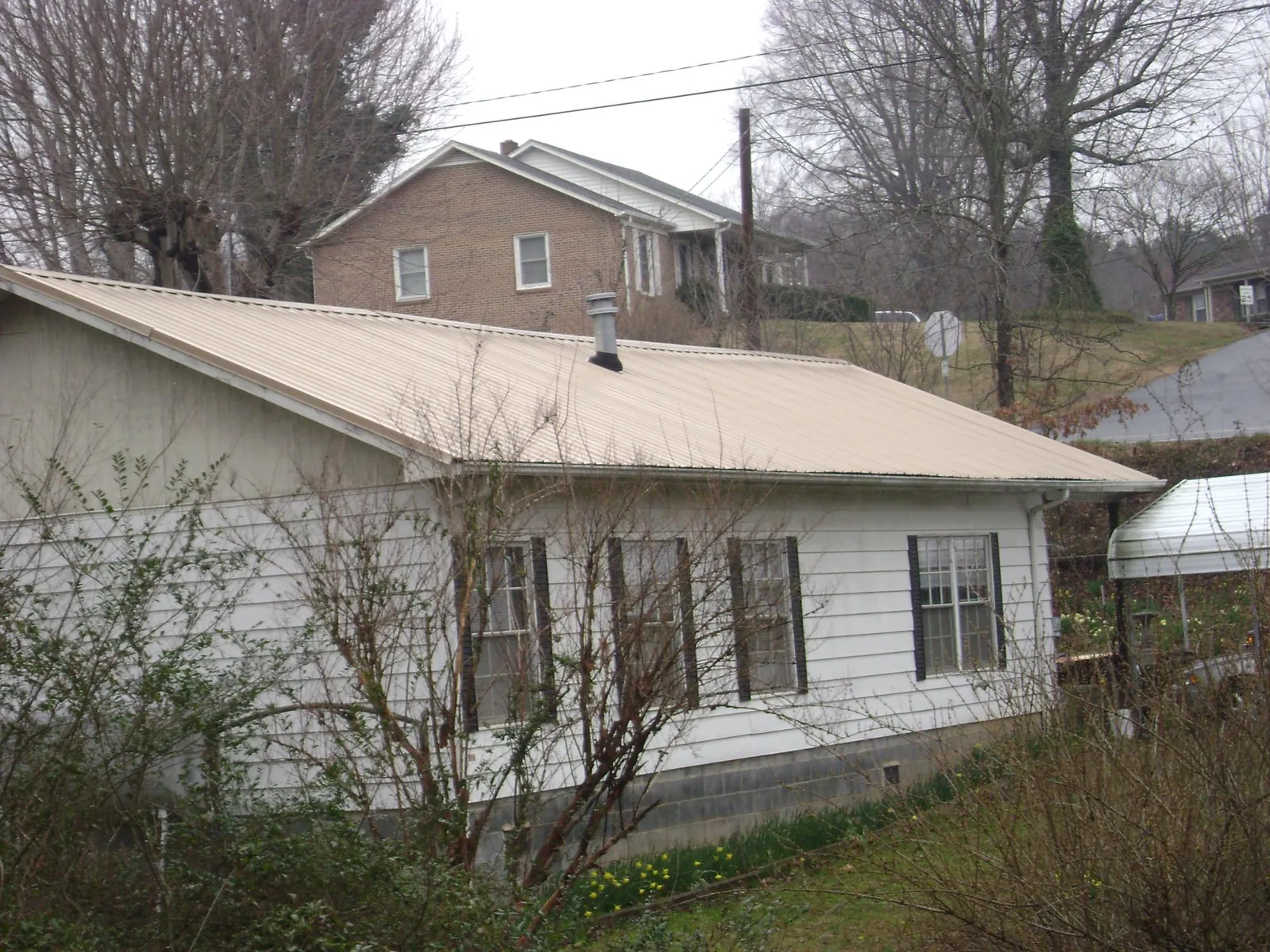 Tan metal roof on a white sided house set into a hillside — Commercial Roofing by Roofing Brothers in Hammondsport