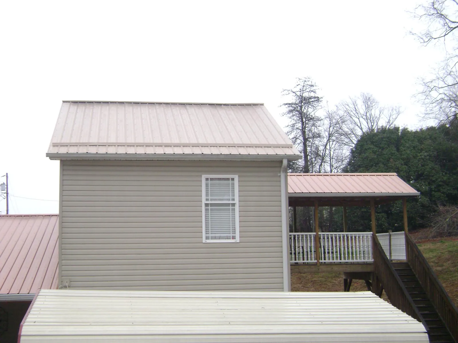Tan metal roofs on a two story addition and attached porch, from a Roof Replacement job in Hammondsport